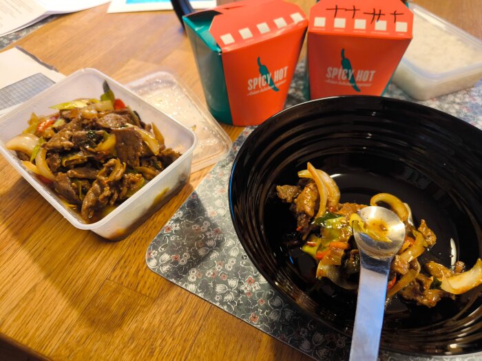 Takeaway från Spicy Hot med kött, lök och grönsaker i en skål och plastlåda på ett bord.