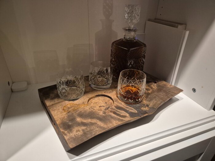 Kristallglas och en karaff på ett träunderlägg, innehållande Diplomatico-rom, placerad i en vit hylla.