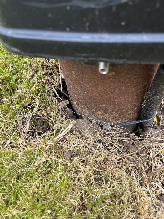 Jordomsluten rostig metallpelare i gräs med svart plast ovanpå och en kapslad kabel bredvid.