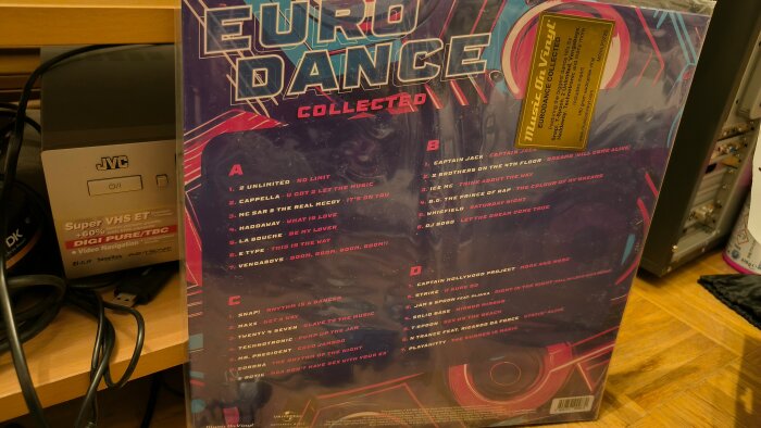 Baksidan av vinylalbumet "Eurodance Collected" med låttitlar från 90-talet, fotograferad bredvid en JVC Super VHS-spelare på en hylla.