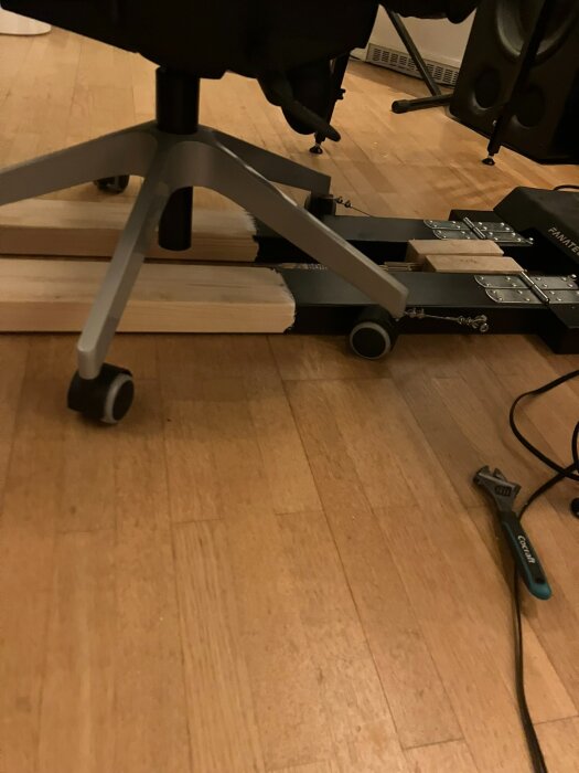 Kontorsstol på hjul ovanpå två träreglar med skruvförband, rörtång vid sidan.