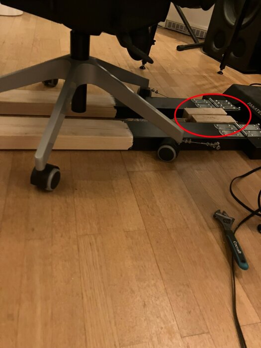Kontorsstol på hjul ovanpå träreglar, med gångjärn och en tumstock. Verktyg ligger bredvid på trägolv.