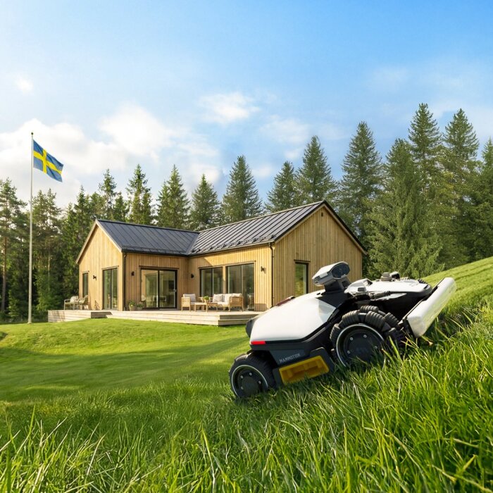 Robotgräsklippare Luba mini 2 AWD från Mammotion klipper gräs på en sluttande gräsmatta framför ett modernt trähus med svensk flagga i bakgrunden.