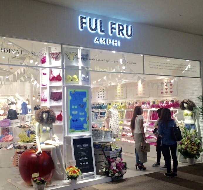 Skyltfönster till butik med namnet "FUL FRU AMPHI", med underkläder och dekorationer. Tre personer tittar in genom glaset.