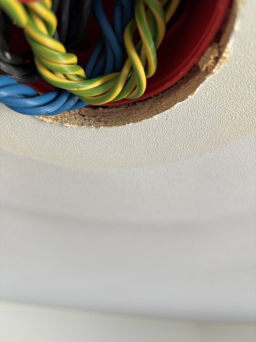 Hål i taket med synliga elkablar och en kant av komprimerat trä efter borttagen takkrok.
