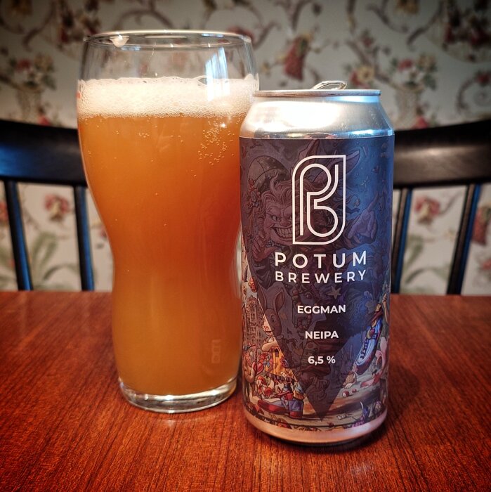 Ölglas med grumlig dryck bredvid en dekorerad ölburk från Potum Brewery, Eggman NEIPA 6,5%, på ett träbord.