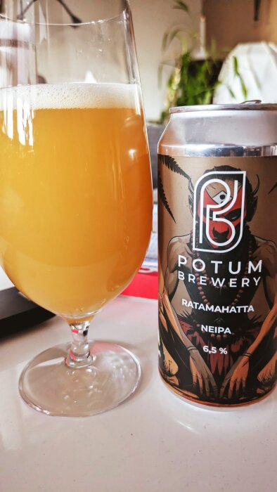 Ett glas med orangefärgad öl bredvid en burk från Potum Brewery, etikett med texten "Ratamahatta NEIPA 6,5%", illustrerad med en figur.