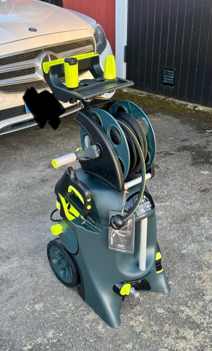 Högtryckstvätten AVA Evolution P80 L-bundle står framför en bil, med sladdrulle och tillbehör i klart gult och svart.