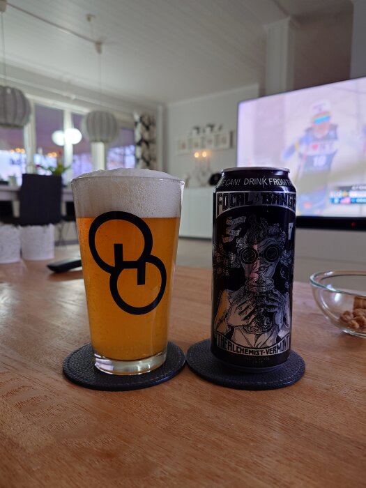 En ölburk märkt "Focal Banger" bredvid ett ölglas med skummande öl, placerad på ett bord i ett modernt vardagsrum.