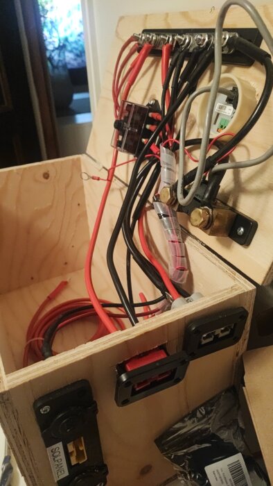 Trälåda med kablage och olika kontakter för ett DIY energisystem, inklusive röda och svarta kablar, med säkringar och Anderson-kontakter monterade.