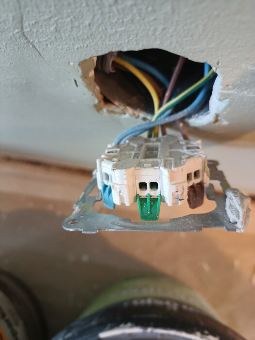 Elektrisk installation bakom ett uttag med synliga kablar, inklusive jordad kabel.