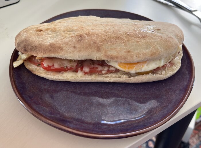 Panini serverad på tallrik med tomat, smält ost och stekt ägg.