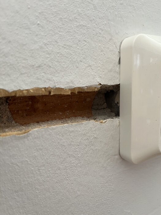 Vägg med ett horisontellt spår för elinstallation och en vit elkontakt.