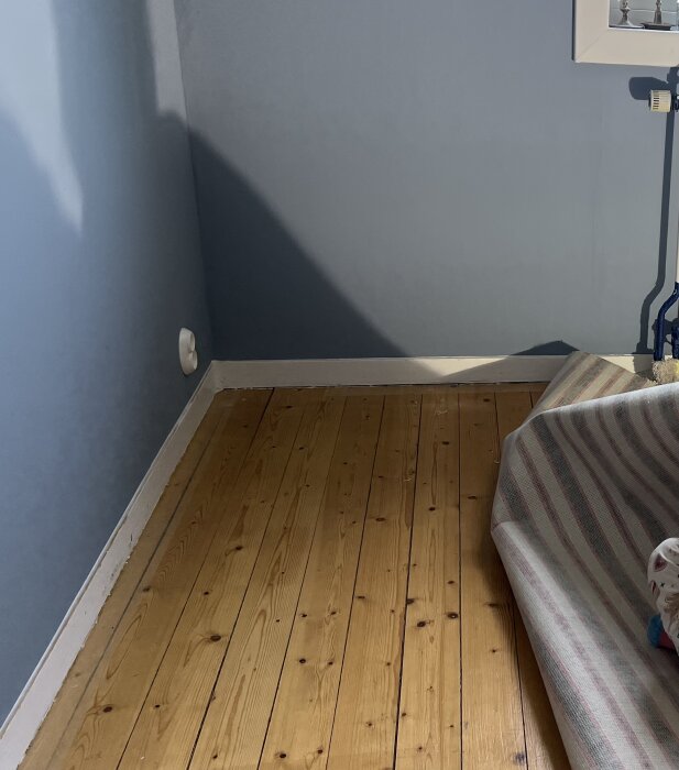 Gammalt brädgolv i sovrum, golvet är delvis blottat under en uppvikt heltäckningsmatta; fråga om behandling och slitning av träytan diskuteras.