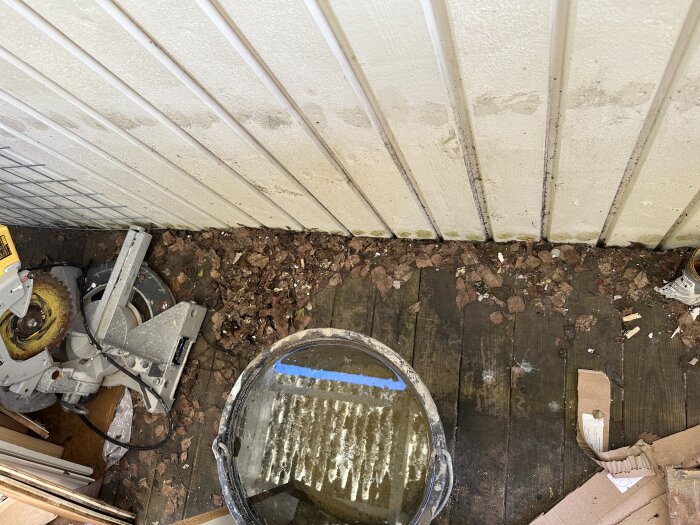 Gammal altan med träväggar, golv och mögelfläckar. Verktyg och lövhögar ligger på golvet. Omtänksam renovering önskas.
