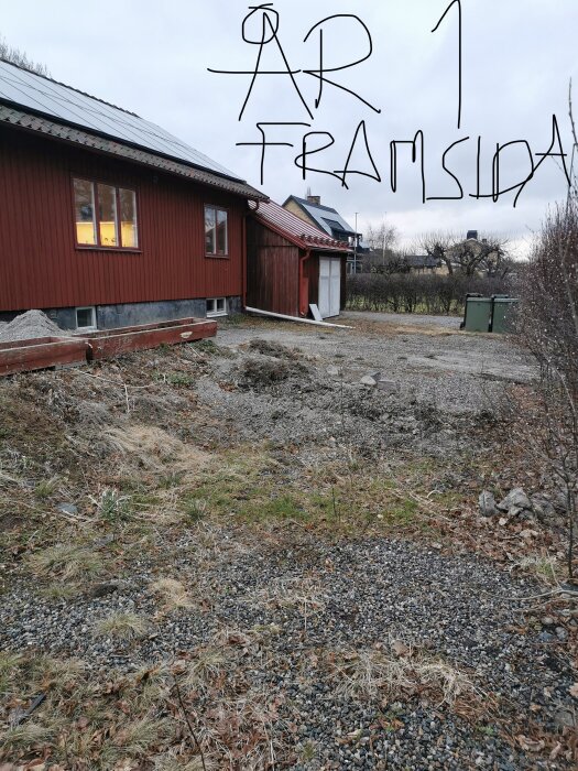 Framsidan av ett rött hus med grusbeläggning och överväxt trädgård, med texten "ÅR 1 FRAMSIDA" skriven över bilden.