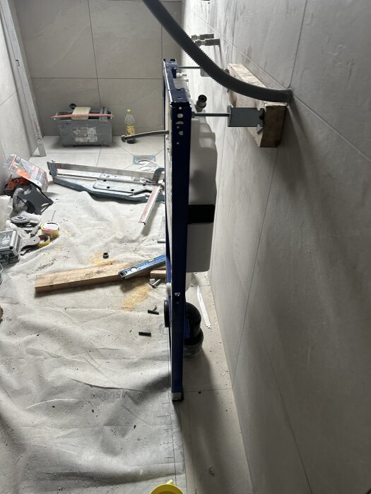 Badrumsrenovering pågår med fixtur monterad på vägg; verktyg och material ligger utspridda på golvet.