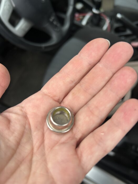 En hand håller i en liten metallbricka, bakgrund visar bilens inre interiör.