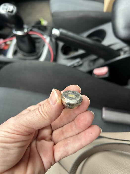 Hand håller metallskruv i bilens framsäte, eventuellt fel skickad produkt jämfört med beställning.