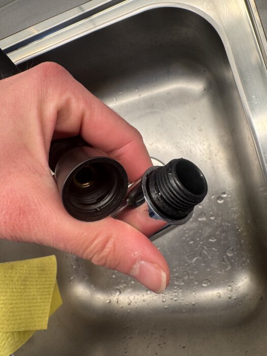 Hand som håller en köksblandare delar och en adapter ovanför diskho.