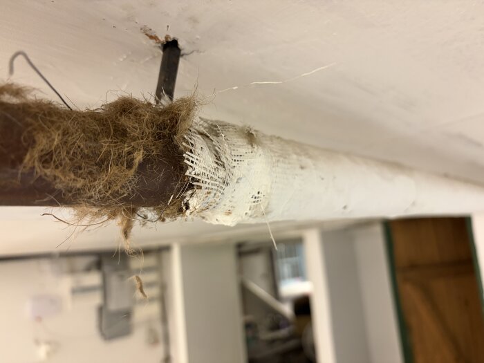Isolering på vattenrör i källare, delvis täckt med fiberliknande material. Eventuell asbestrisk bedöms för provtagning.