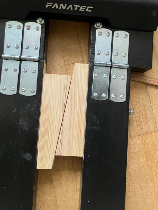 Två träbitar fastkilade diagonalt mellan två svarta ställningar med gångjärn, del av byggprojekt för att justera reglar.