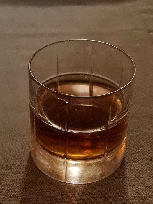 Ett whiskyglas med bärnstensfärgad vätska står på ett brunt bord.