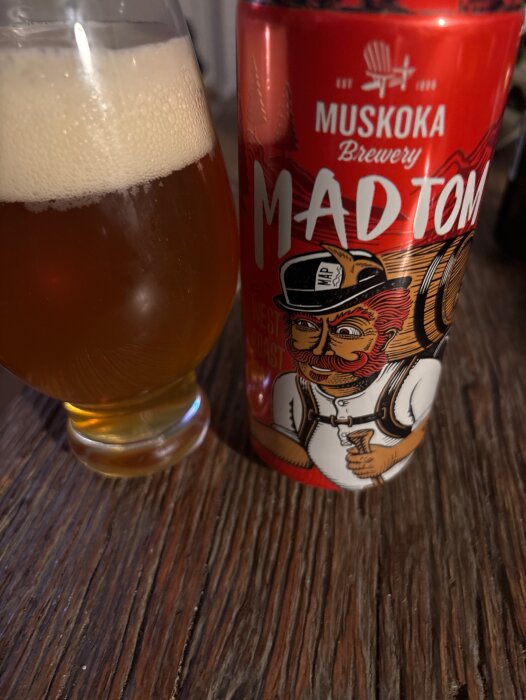 Ölglas med skum bredvid en Mad Tom-burk från Muskoka Brewery på ett träbord.