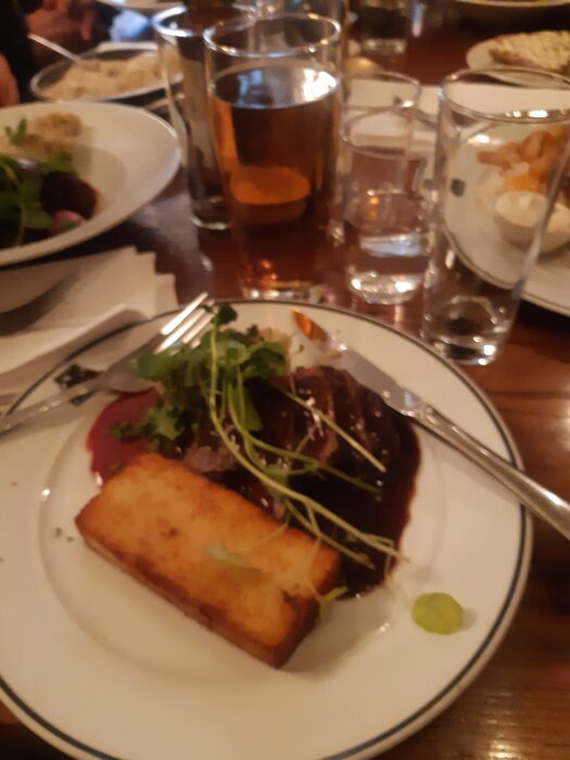 Kryddstekt hjortinnanlår med grönsaker och stekt potatisbröd på tallrik, serverad med dryck på restaurang Pelikan.