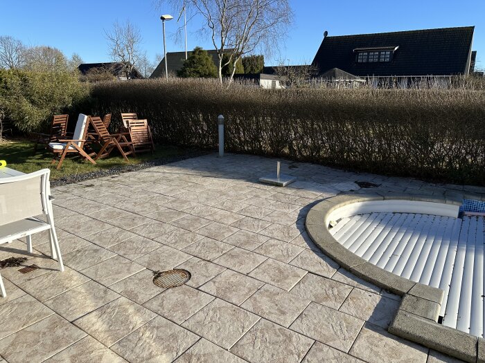 Uteplats med trädgårdsmöbler och en rund pool, omgiven av häckar och en stenlagd yta.