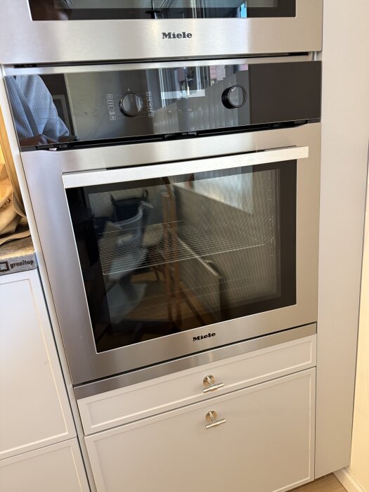 Rostfri Miele inbyggnadsugn med digital display och vred, installerad i kök med vita skåpluckor.