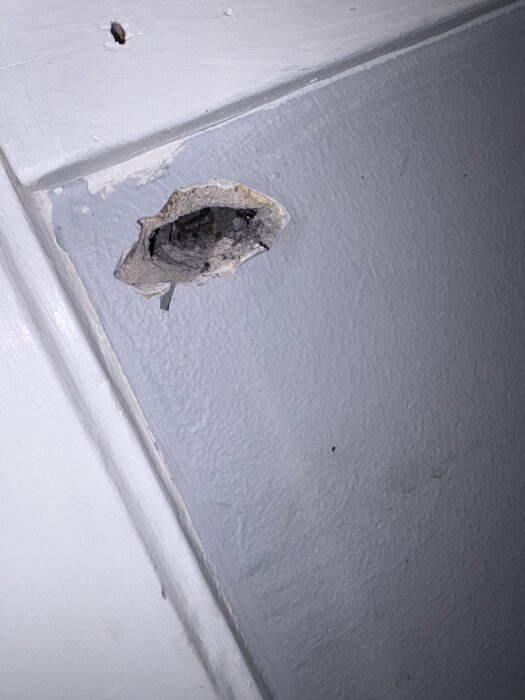 Hål i en vägg med poröst stenliknande material synligt, troligen från borrning inför renovering av hall i lägenhet byggd 1929.