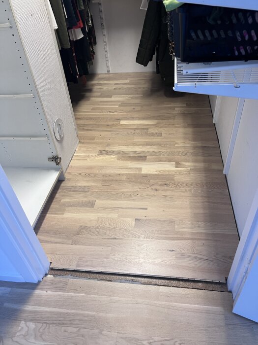 Nyinstallerad parkettgolv i en klädkammare med ljus träfinish, kläder synliga i bakgrunden.