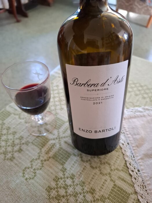 En flaska rödvin, Barbera d'Asti, och ett glas vin står på ett bord.
