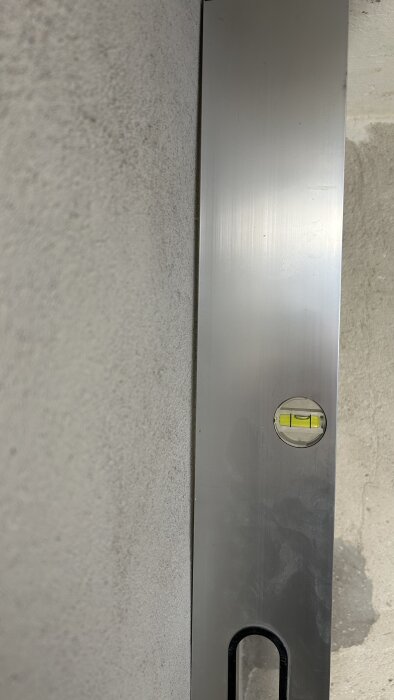 Ett vattenpass mäter jämnheten på en putsad källarvägg, visar avvikelse på cirka 1 cm över 2 m.
