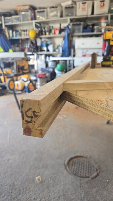 Träbord under konstruktion i ett garage med en plywoodskiva och trästavar, del av ett pågående gör-det-själv-projekt med epoxy och teaklista.