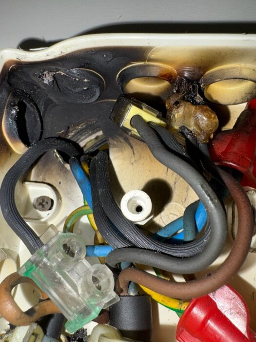 Bränt eluttag med smält plast och sotiga kablar från överhettning eller kortslutning, visar elektrisk skada och potentiella säkerhetsrisker.