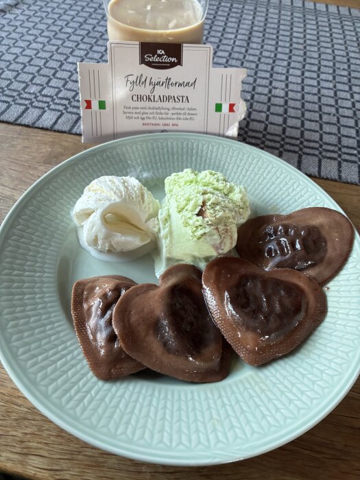 Tallrik med hjÀrtformad chokladpasta, vanilj- och pistageglass, samt ett glas med dryck.