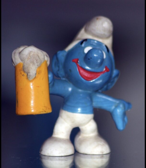 Blå leksaksfigur håller ett gult ölglas med vitt skum.