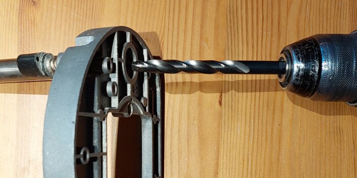 Bilden visar en borrmatad drill som borrar genom basen av en metallplatta, en del av en DIY-höjdjustering för en fräsinstallation.