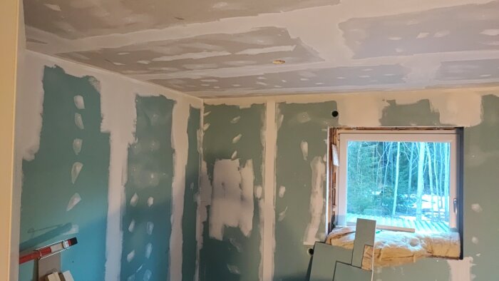 Rum med gipsskivor på väggar och tak, spacklade skarvar och fönster sett utifrån under renovering.