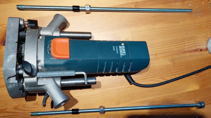 En Black & Decker fräs ligger upp och ner med två gängstänger bredvid, på ett trädäck, redo för justering och montering i en bordfräs.