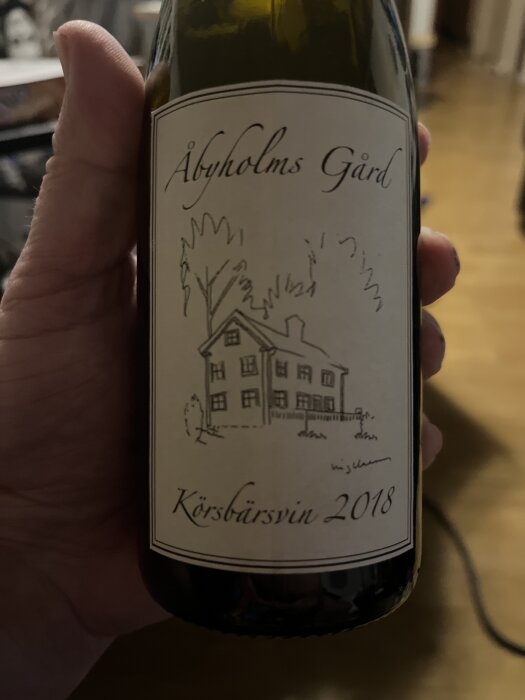 Flaska märkt "Åbyholms Gård Körsbärsvin 2018" hålls i en hand.