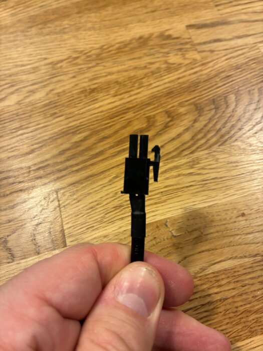 En hand håller i en svart kabel med kontakt mot en träyta, relaterad till diskussion om drivrutiner för badrumsspottar.
