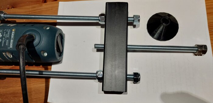 Hemmagjord bordfräslösning med Black & Decker-fräs, tre gängstänger, fyrkantigt stålrör och svart 3D-printad stödhylsa på träyta.