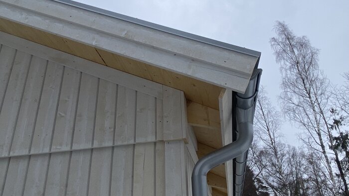 Vitmålad takfot med synlig takstol och hängränna, del av husets fasad, omgiven av kala träd, diskuteras för montering av markis.