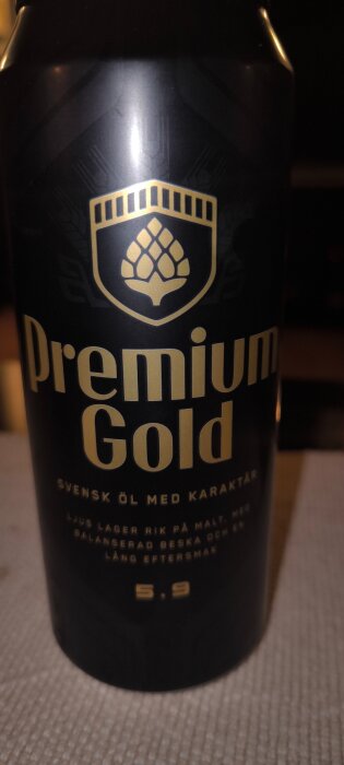 Svart ölburk med guldtexten "Premium Gold", en humledekoration och text om svensk starköl med karaktär, alkoholhalt 5.9%.
