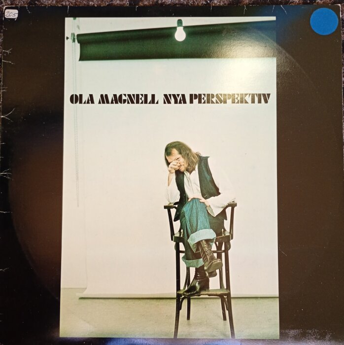 Omslaget till skivan "Nya Perspektiv" av Ola Magnell från 1975. Personen sitter på en stol i ett fotostudio med en lampa ovanför.