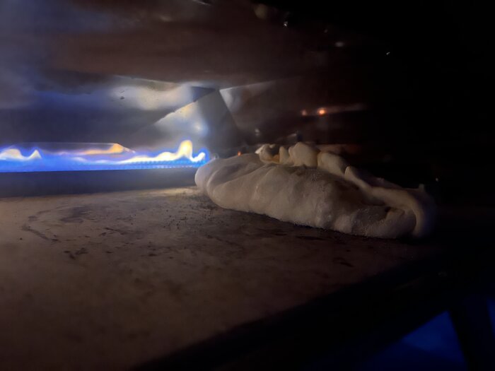 Deg som gräddas i en vedeldad pizzaugn, med blå lågor synliga på insidan av ugnen.