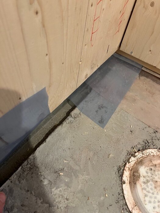 Urgröpning i betongplatta vid badrumsvägg med träpanel och synlig avloppsbrunn. Diskussion om flytspackling och förbättring av fall.